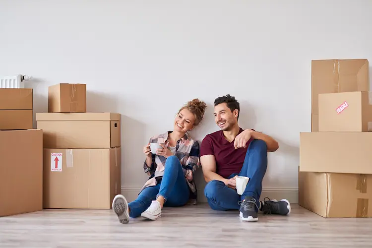 happy couple sitting on floor surrounded by moving boxes