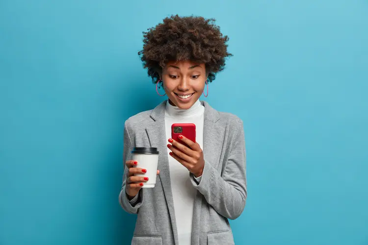 beautiful young woman with cup of coffee looking at phone excited