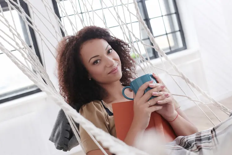 black woman in hammock with cup of tea and book