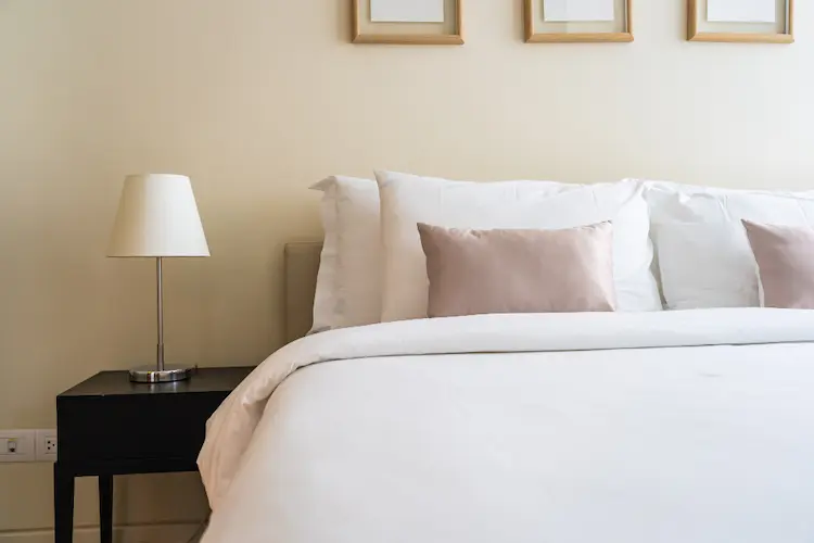 made bed with white bedspread pink and white pillows lamp