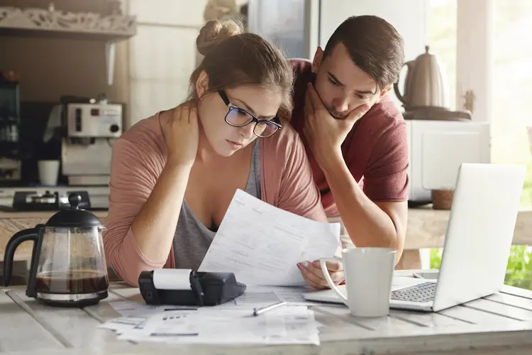 young couple looking at bills and laptop stressed always broke