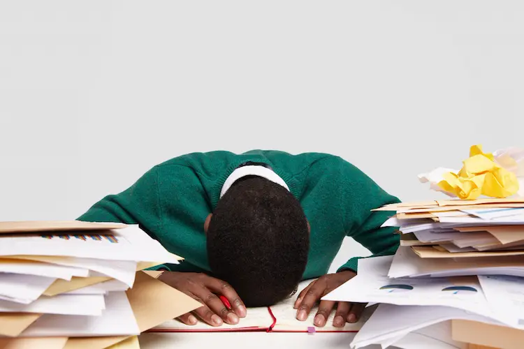 man with head on pile of paperwork