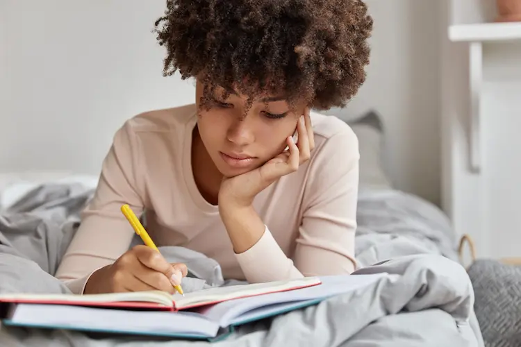 beautiful woman with afro hairstyle writing in journal notebook planner