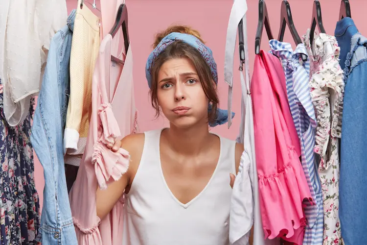 depressed female standing near wardrobe rack full clothes having difficult choice knowing what put