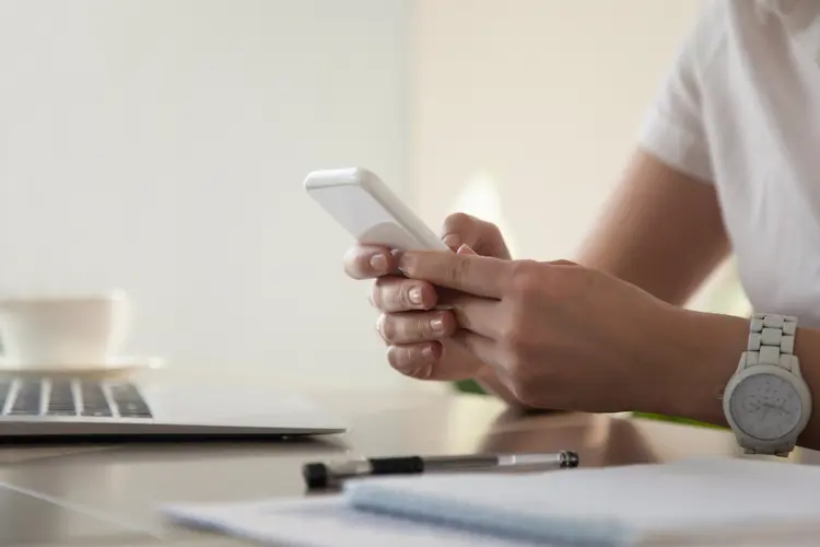 woman holding phone at desk with laptop