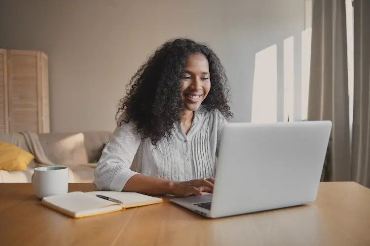 black woman on laptop with cup and notebook