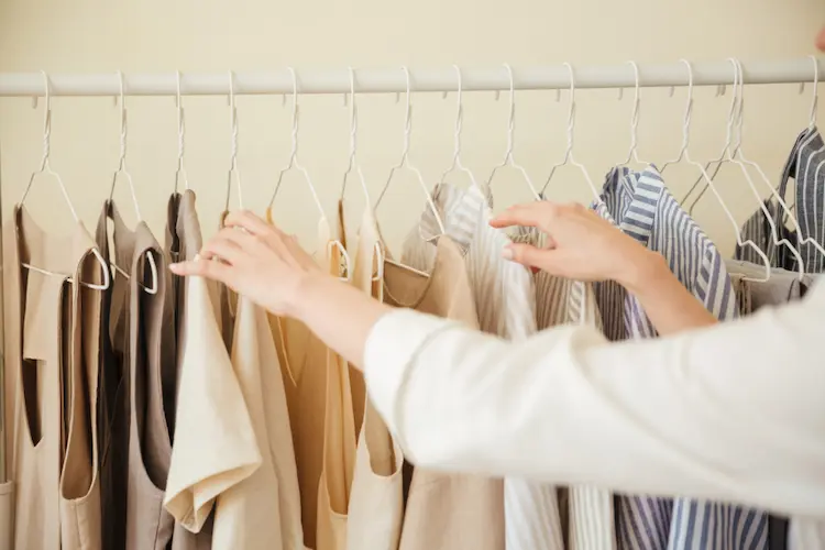 womans hands looking through clothes hanging on rack clothing closet