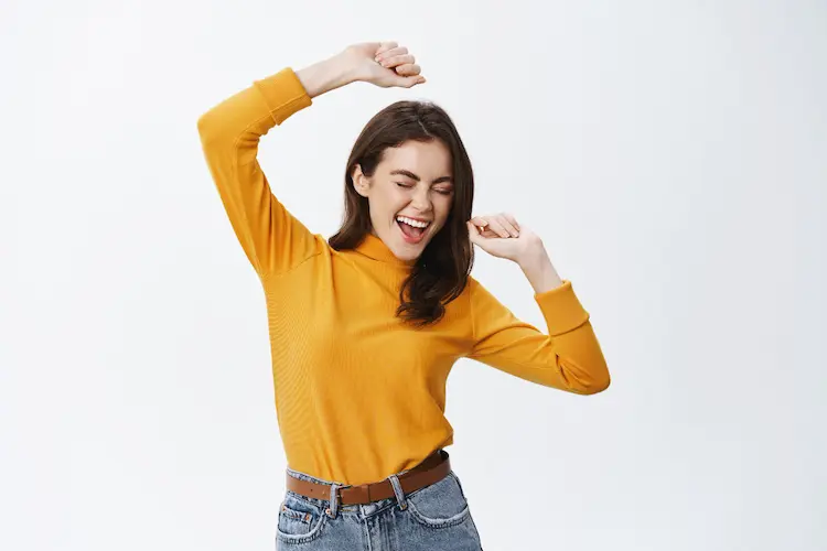 happy attractive woman dancing having fun raising hands up carefree enjoying music standing against white wall