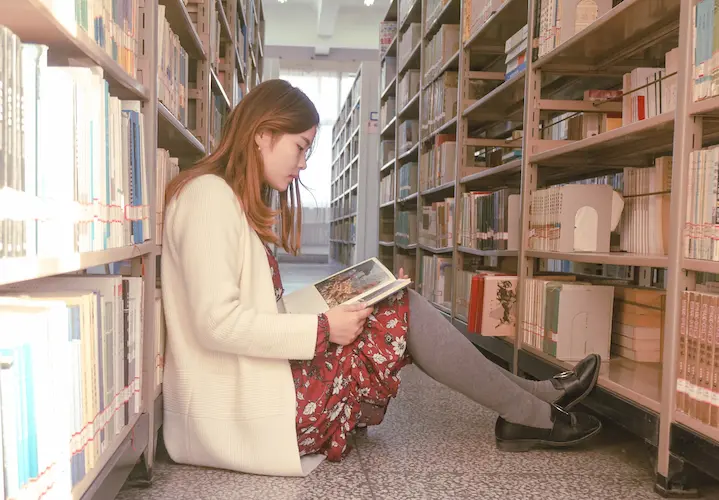 woman sitting on floor reading in library decluttering books 