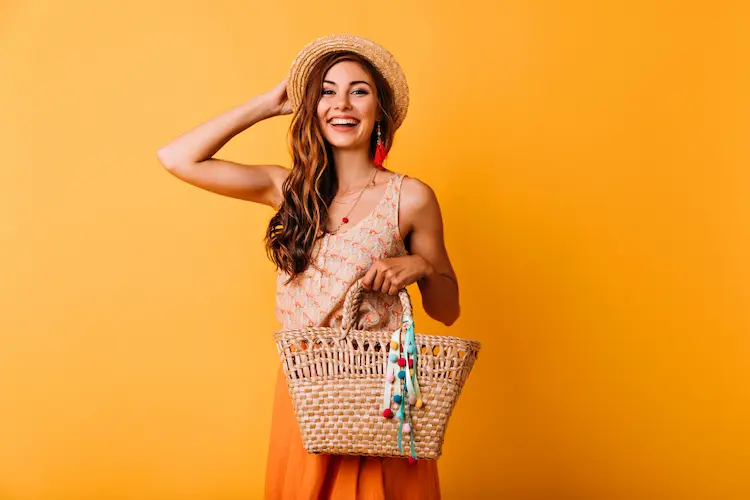 pretty woman in summer clothes with hat and bag orange background