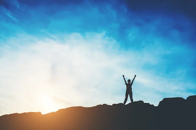 person on top of mountain arms out in victory open air life
