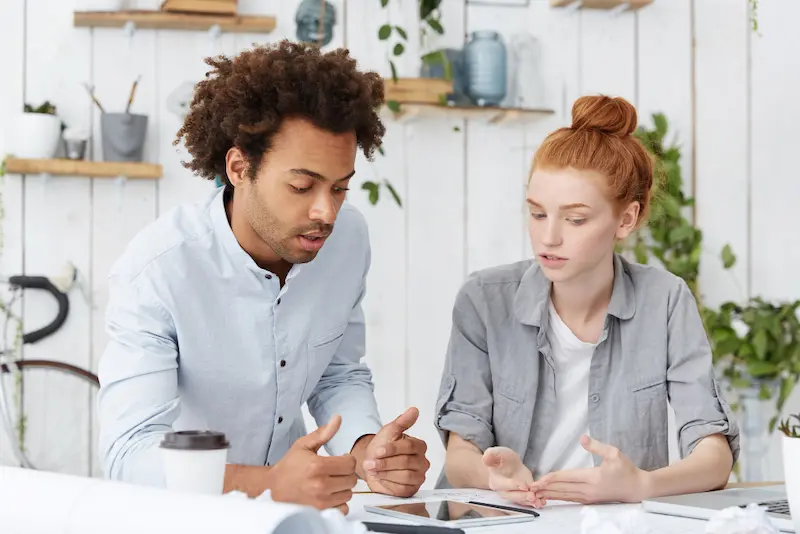 multi ethnic couple or team brainstorming talking at white desk