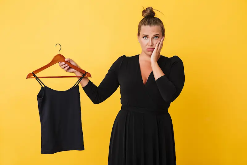 young woman black dress holding too small tank top on hanger